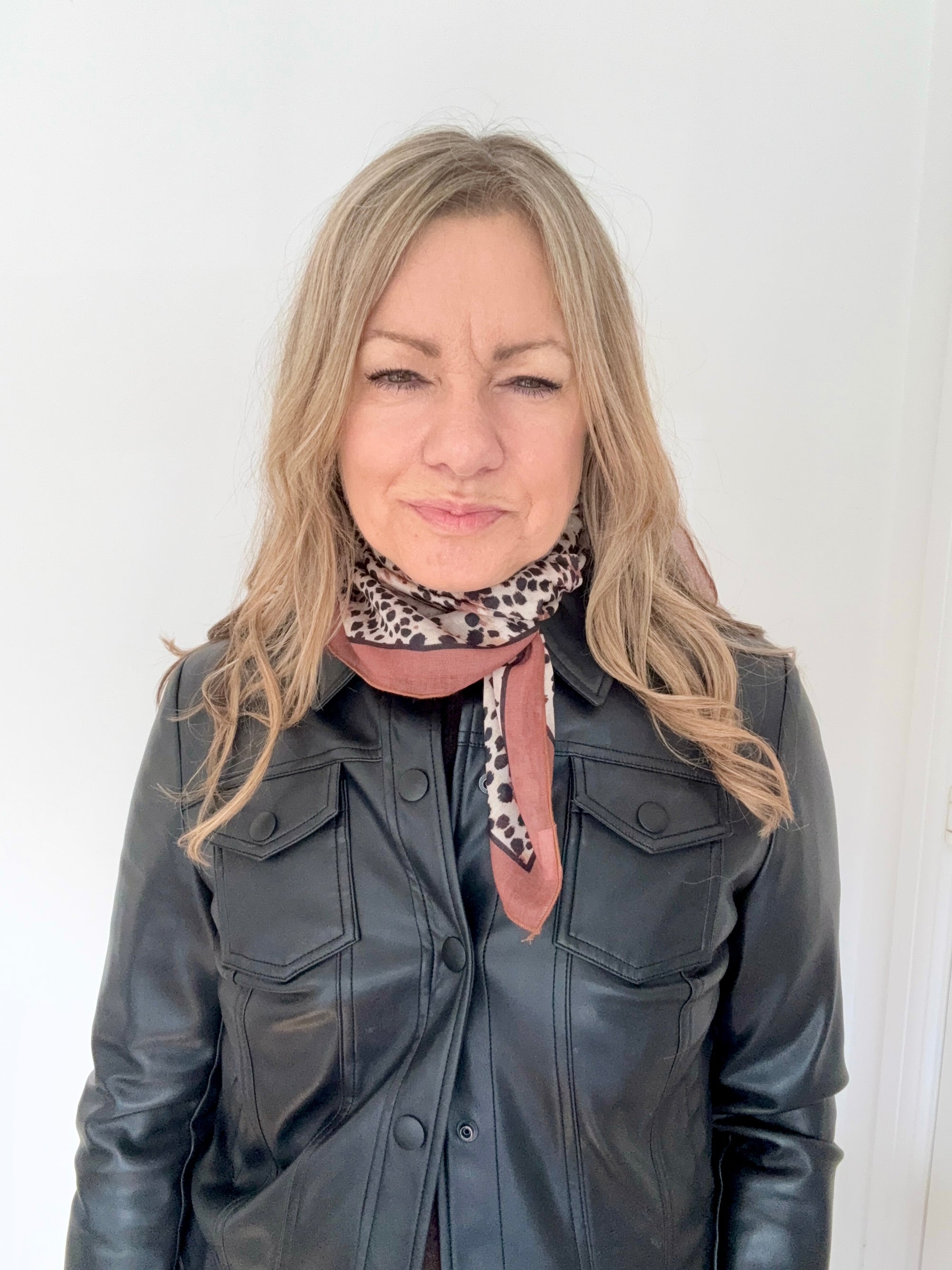 Woman wearing a black leather jacket and a animal print square scarf.