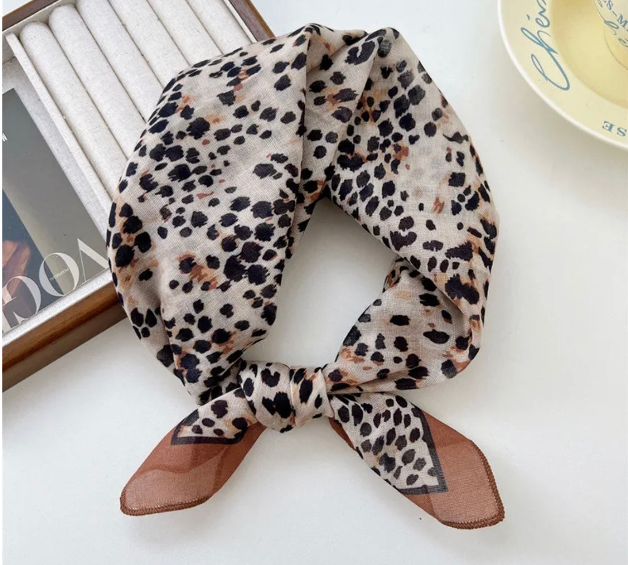 Animal print square scarf tied neatly on a white surface with a magazine in the background.