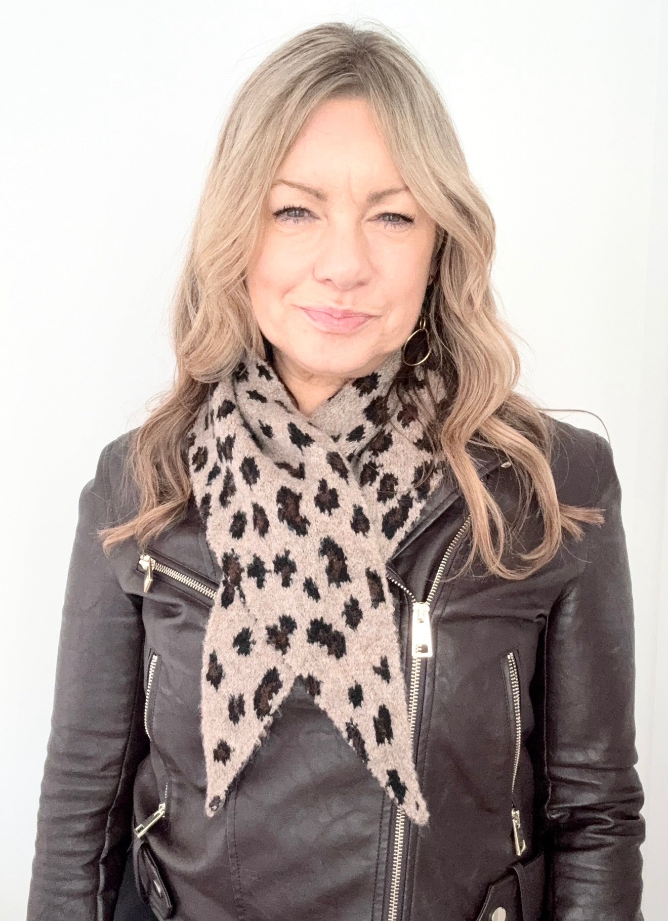 Woman wearing a black leather jacket and a leopard print scarf on a white background