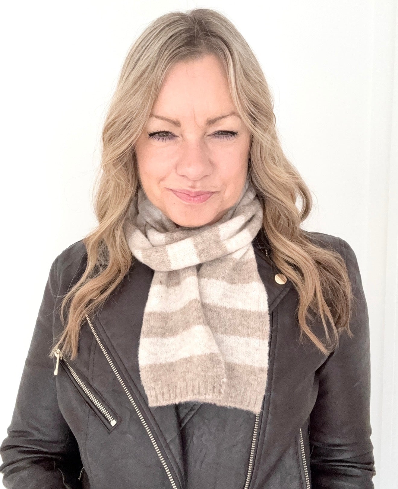 Woman wearing a taupe and cream knitted  striped scarf and leather jacket 