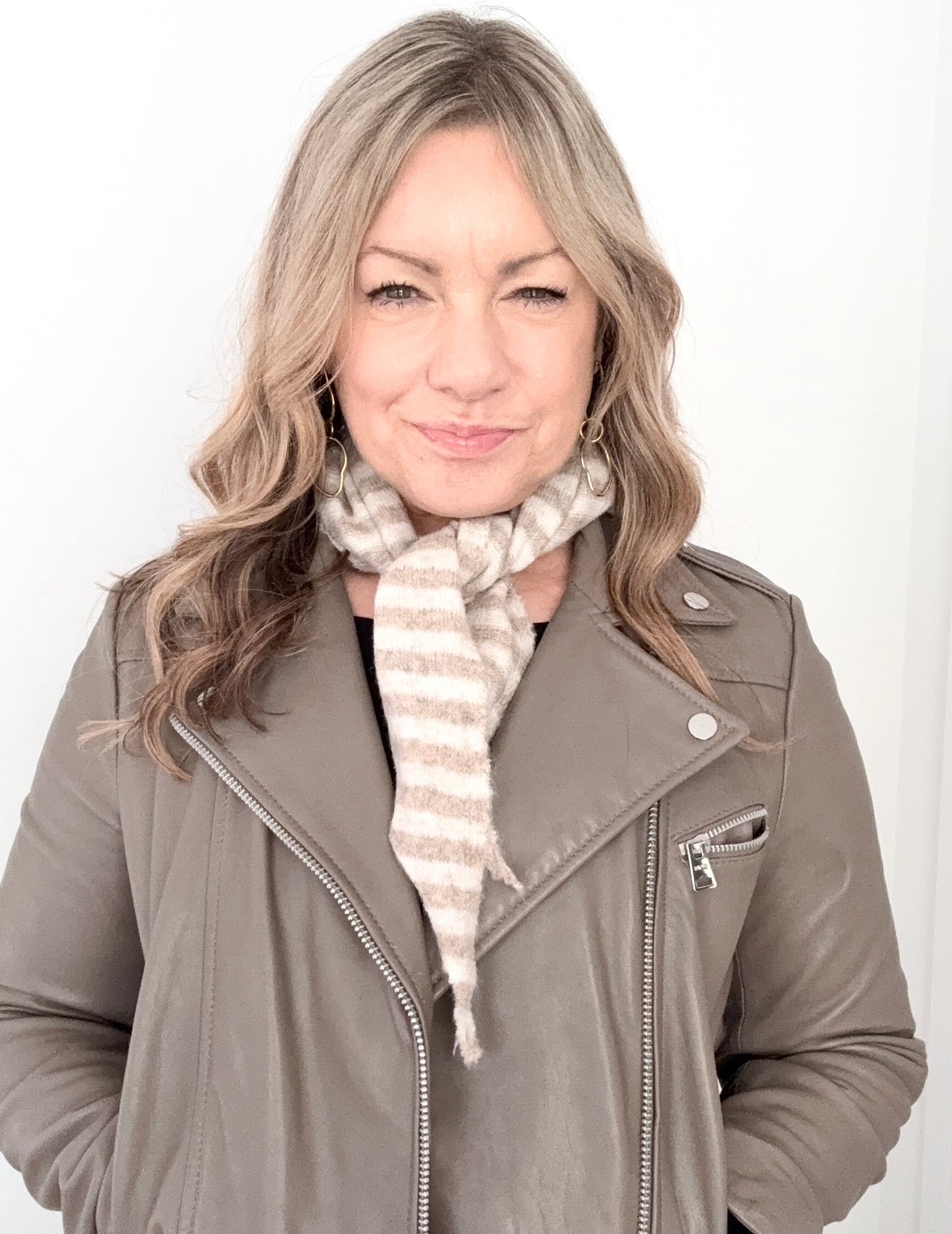 Woman wearing a gray jacket and a taupe and cream striped scarf against a white background