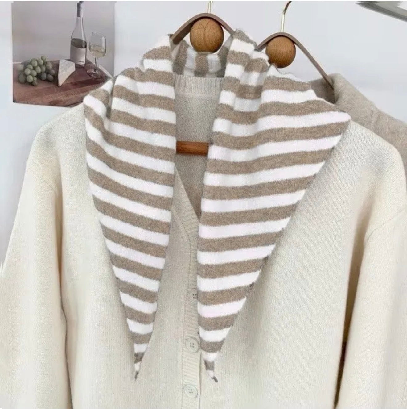 taupe and cream striped scarf draped over a white cardigan on a wooden hanger.