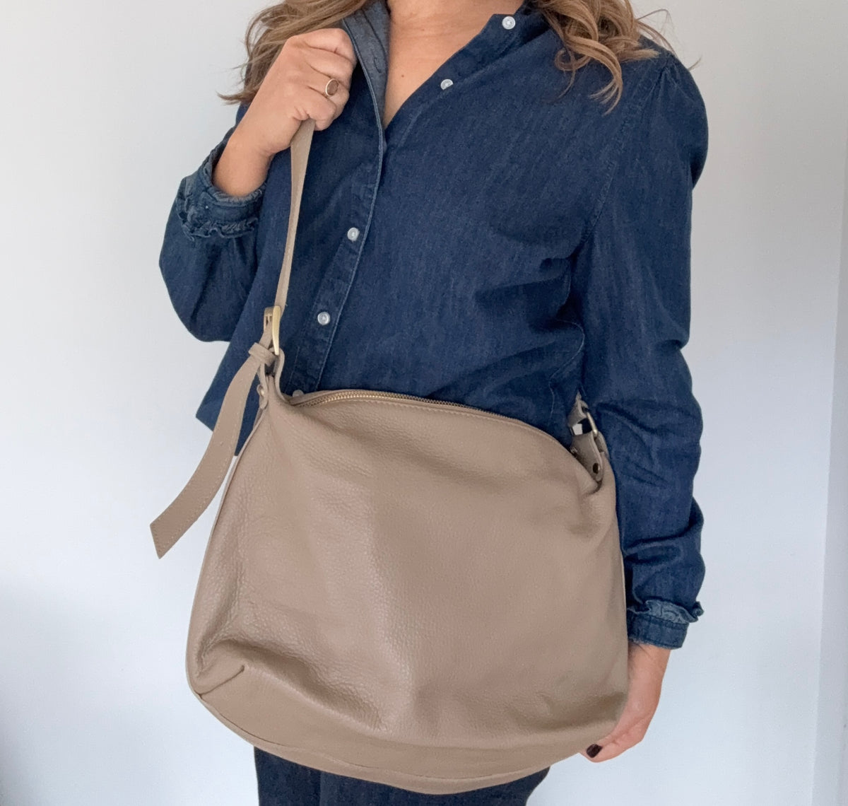 woman wearing a denim shirt, holding a taupe crossbody handbag.