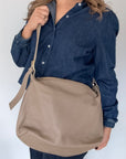 woman wearing a denim shirt, holding a taupe crossbody handbag.
