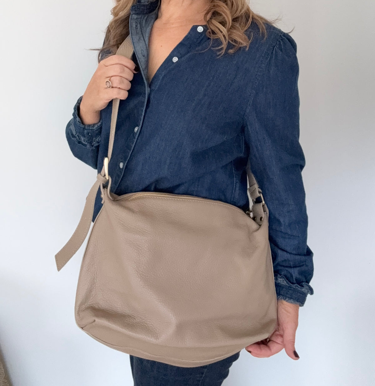 Woman wearing a denim shirt, holding a taupe crossbody handbag.