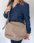 Woman wearing a denim shirt, holding a taupe crossbody handbag.