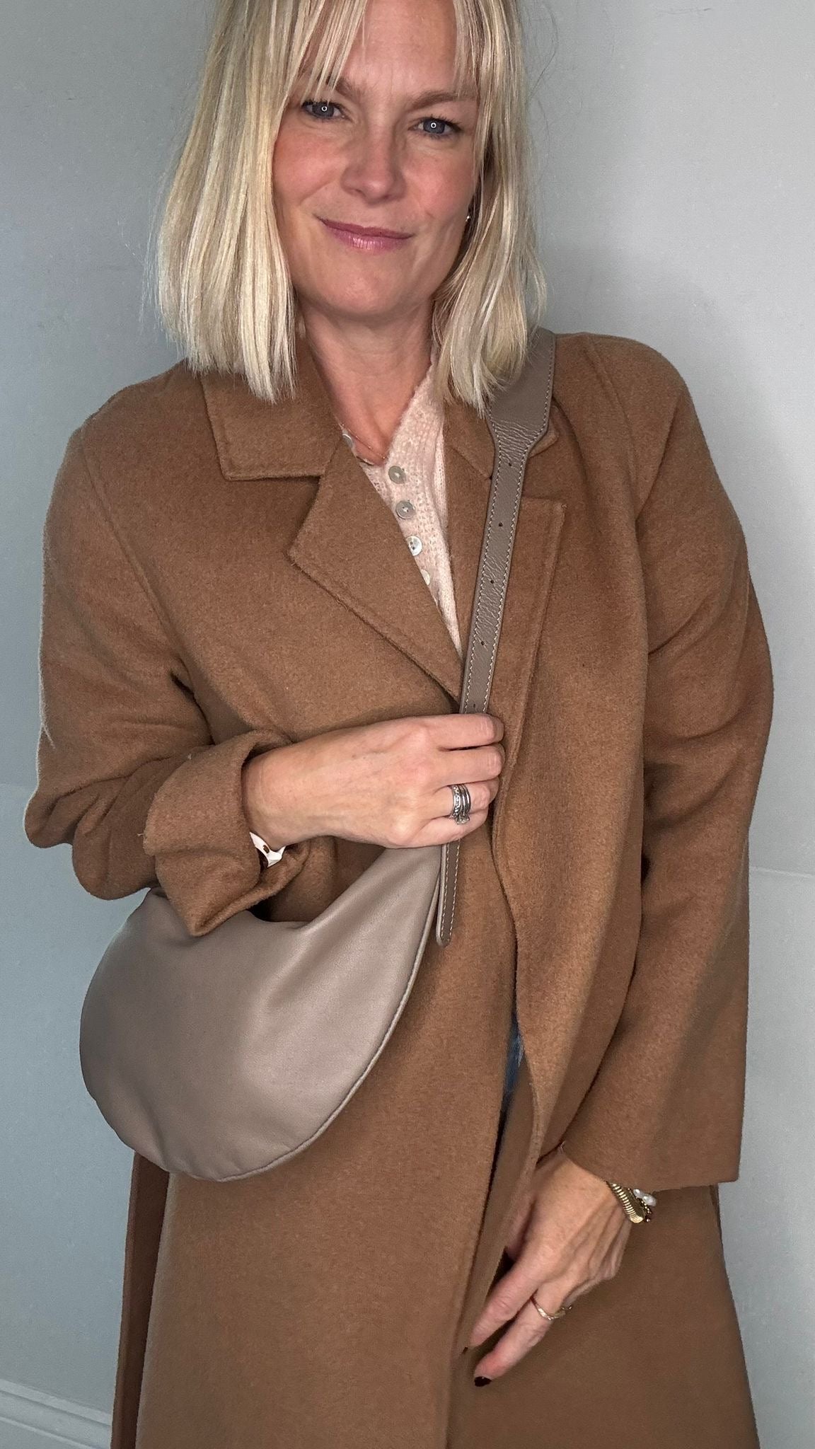 Woman wearing a brown coat holding a taupe crossbody/ shoulder handbag 