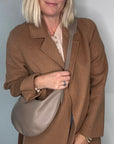 Woman wearing a brown coat holding a taupe crossbody/ shoulder handbag 