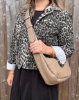 Woman wearing a leopard print jacket holding a taupe crossbody handbag.