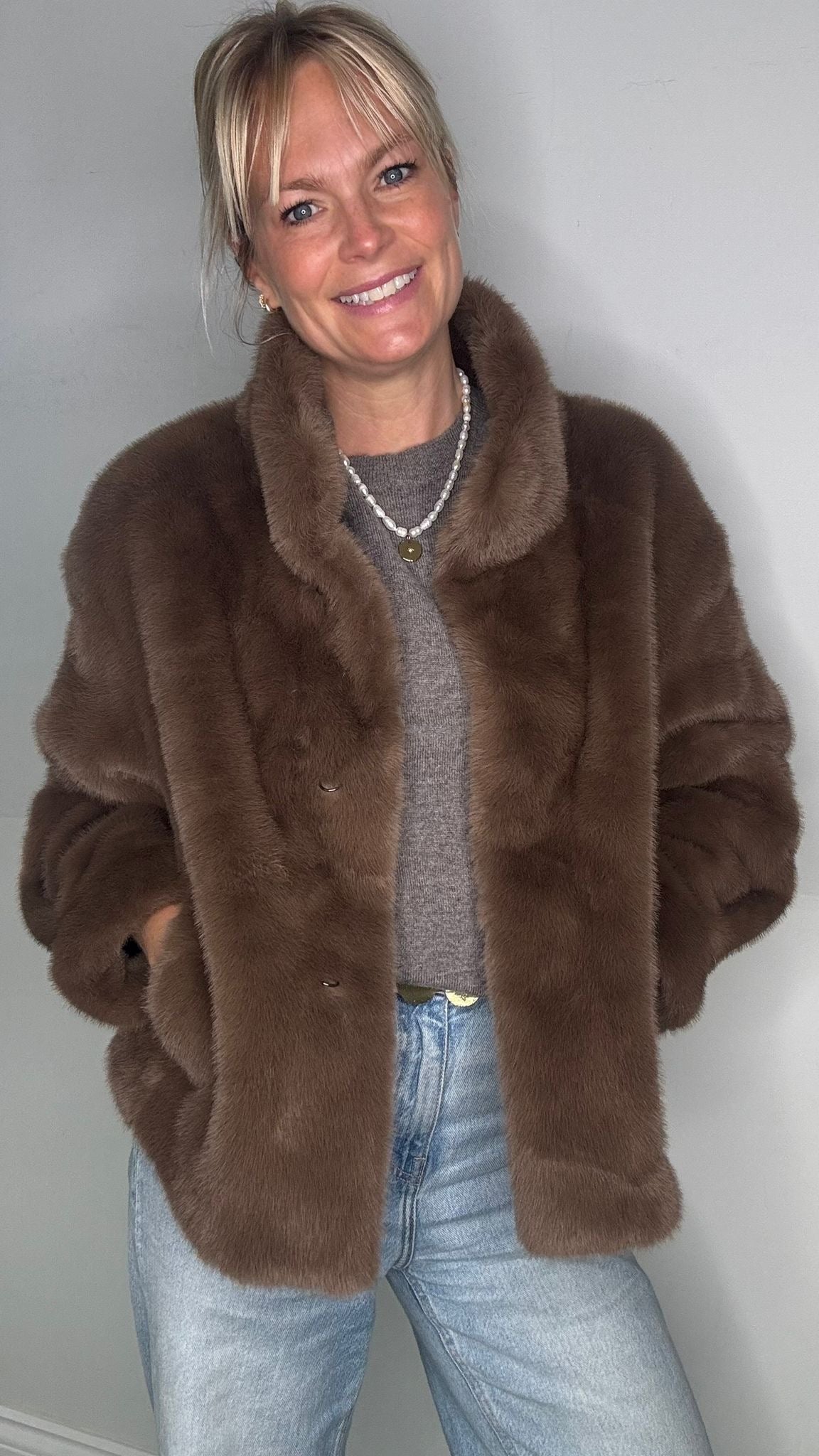Woman wearing a taupe faux fur coat over a grey jumper 