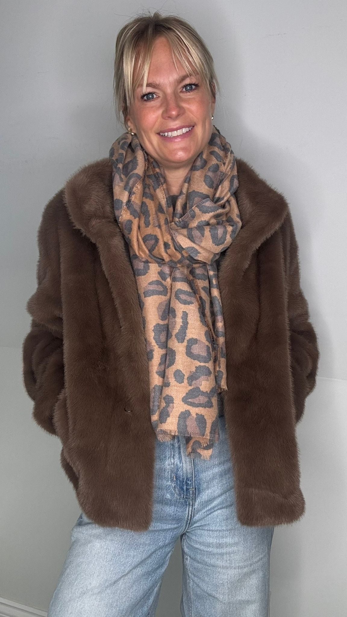 Woman wearing a taupe faux fur coat over a leopard print scarf. 