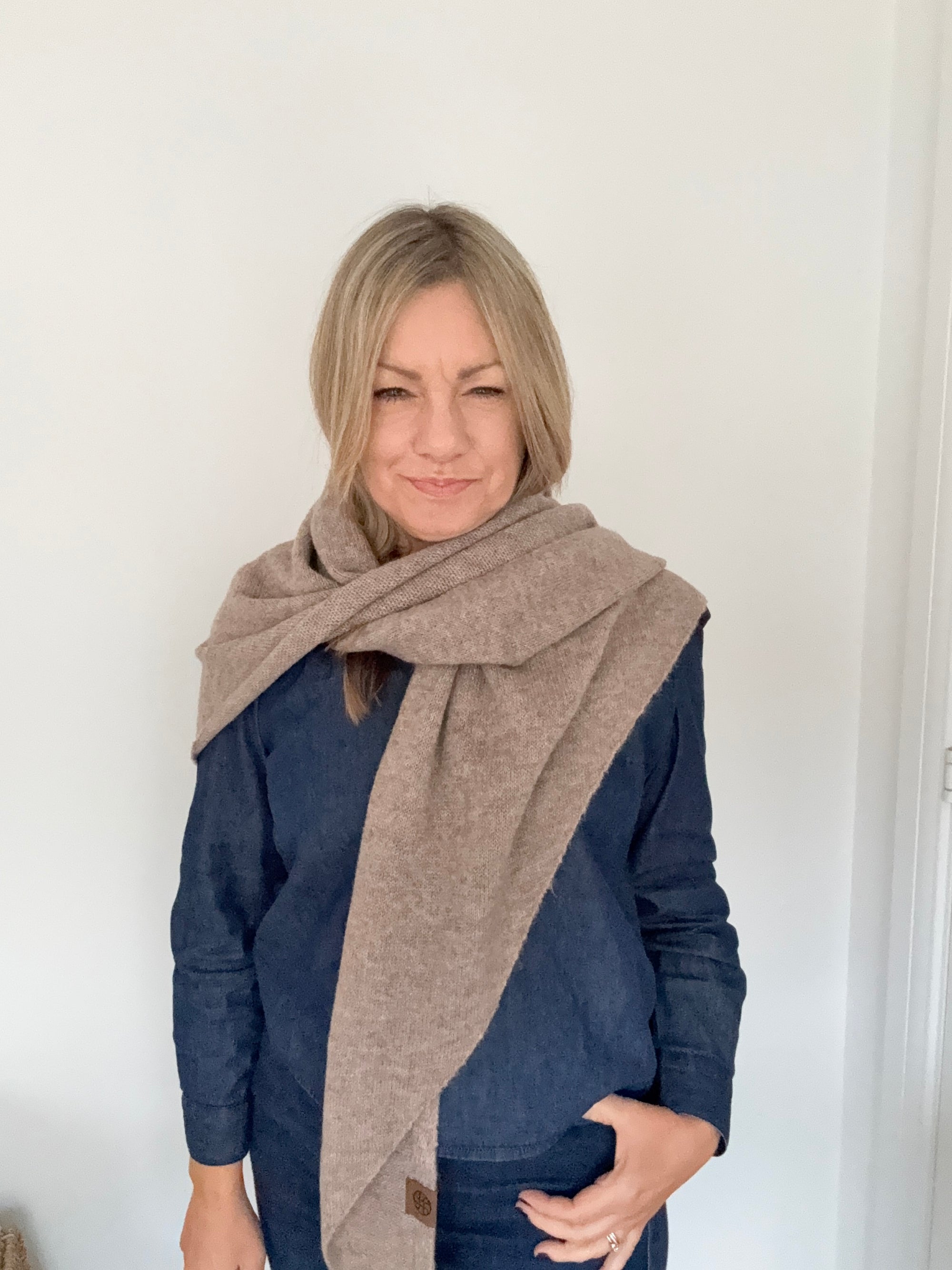 Woman wearing a blue denim outfit with a taupe knit scarf. 