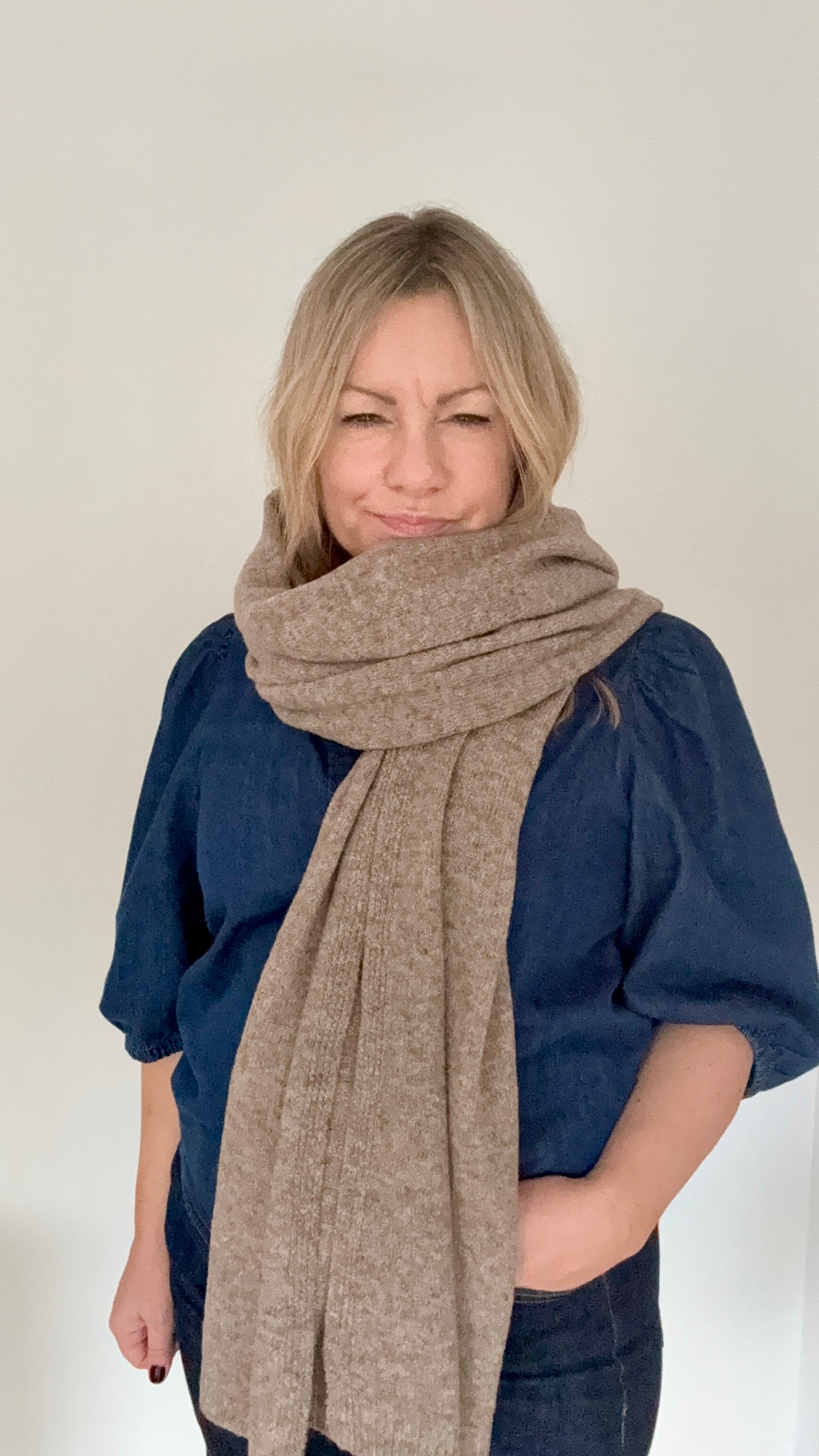 Woman wearing a taupe knitted  scarf and blue top 