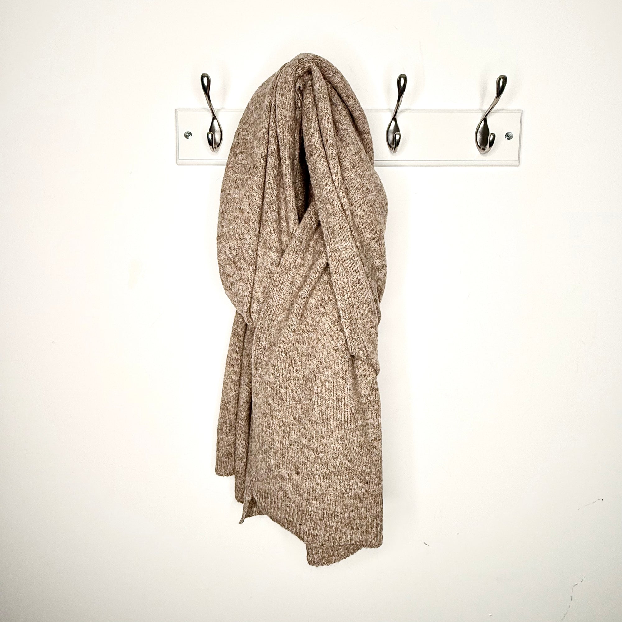 taupe knitted  scarf draped over a hook on a white wall