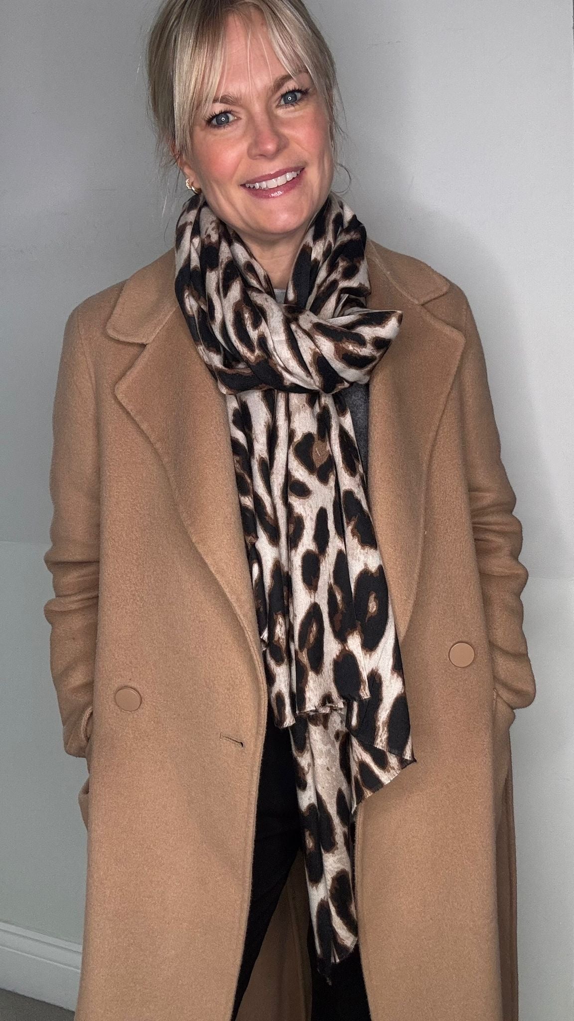 Woman wearing a dark taupe coat,  and a  taupe leopard print scarf 