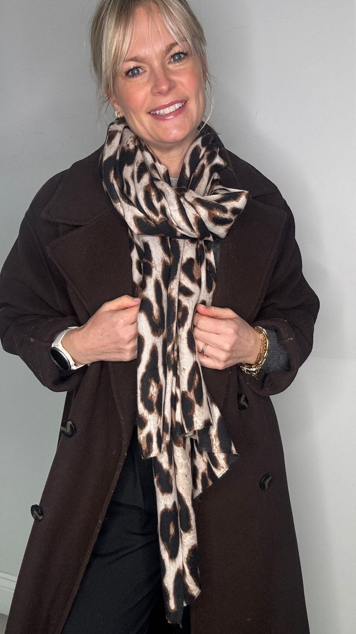 Woman wearing a brown coat and a taupe leopard print scarf 