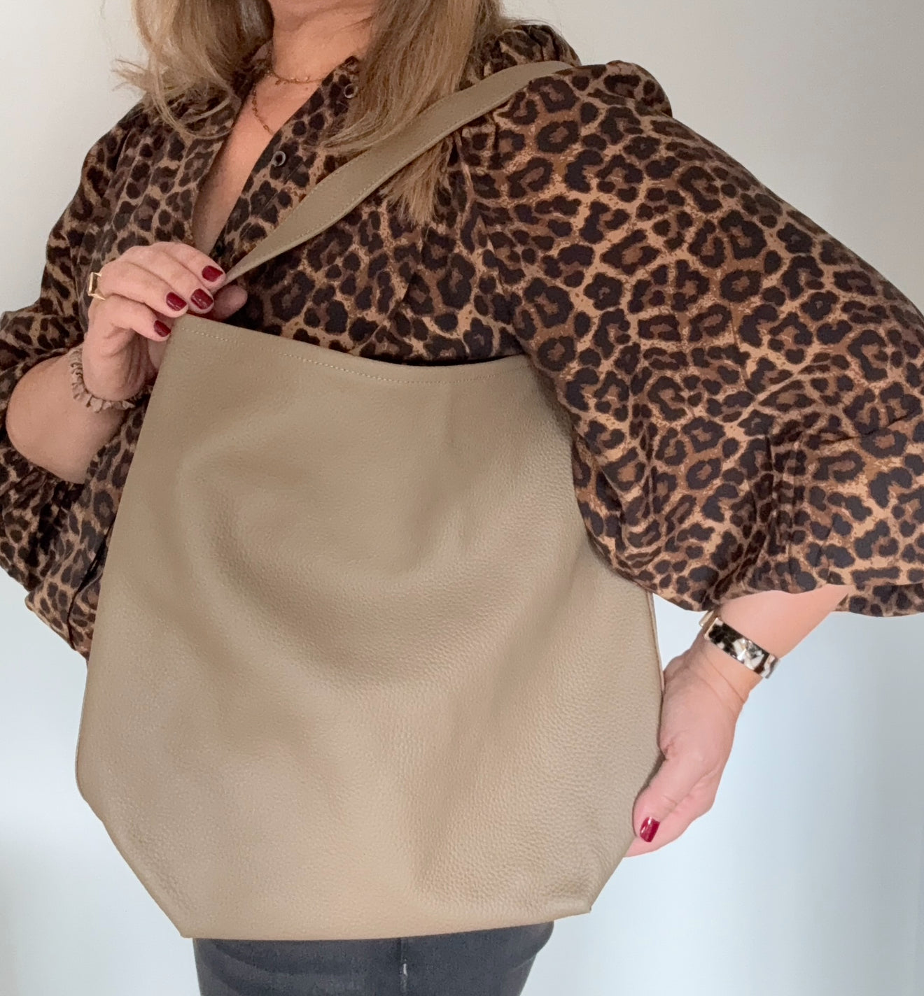 Woman wearing a leopard print top with a beige leather tote bag 