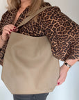 Woman wearing a leopard print top with a beige leather tote bag 
