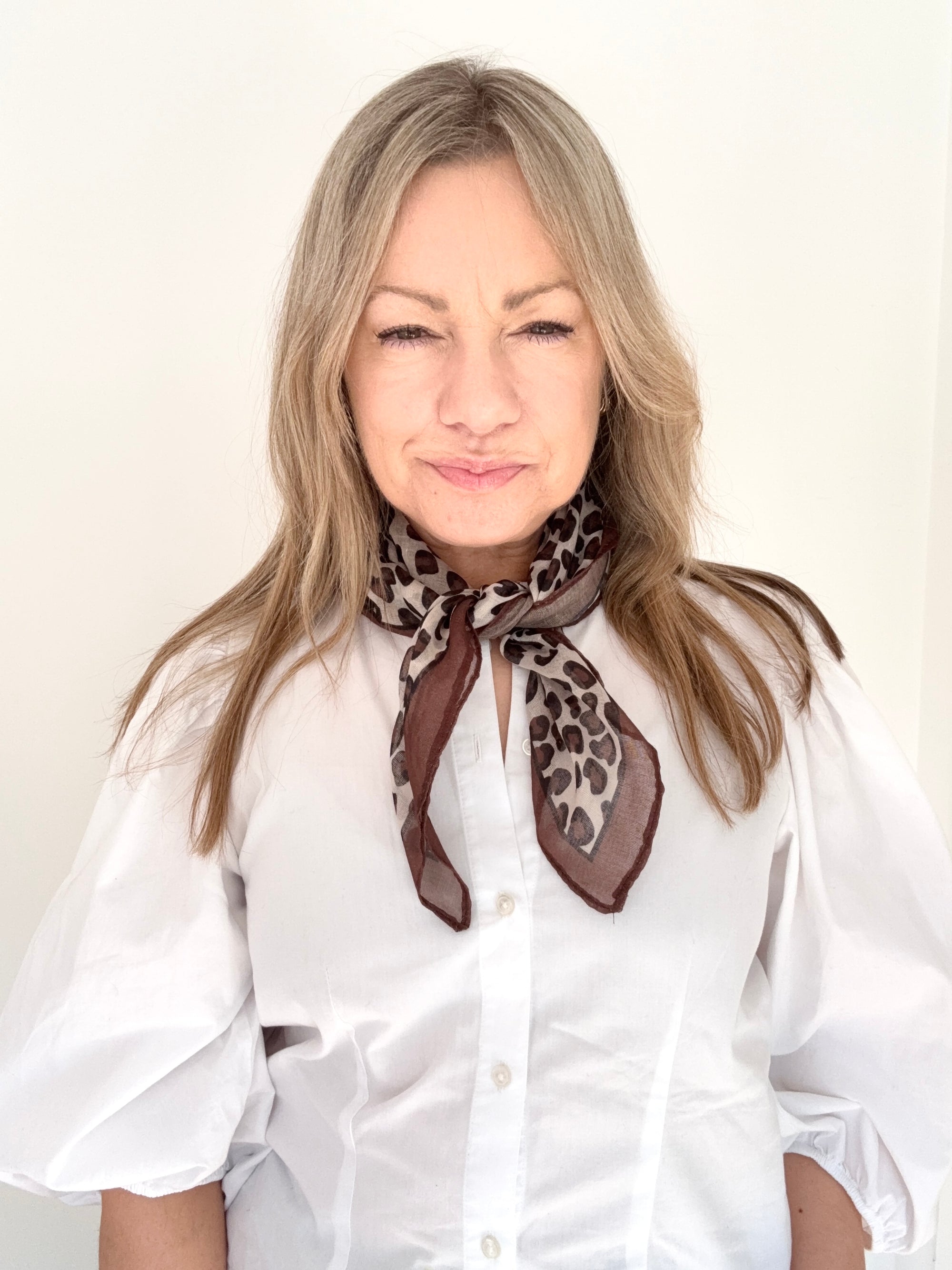 Woman wearing a white shirt and a taupe animal print scarf.