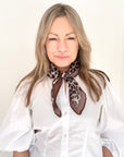 Woman wearing a white shirt and a taupe animal print scarf.