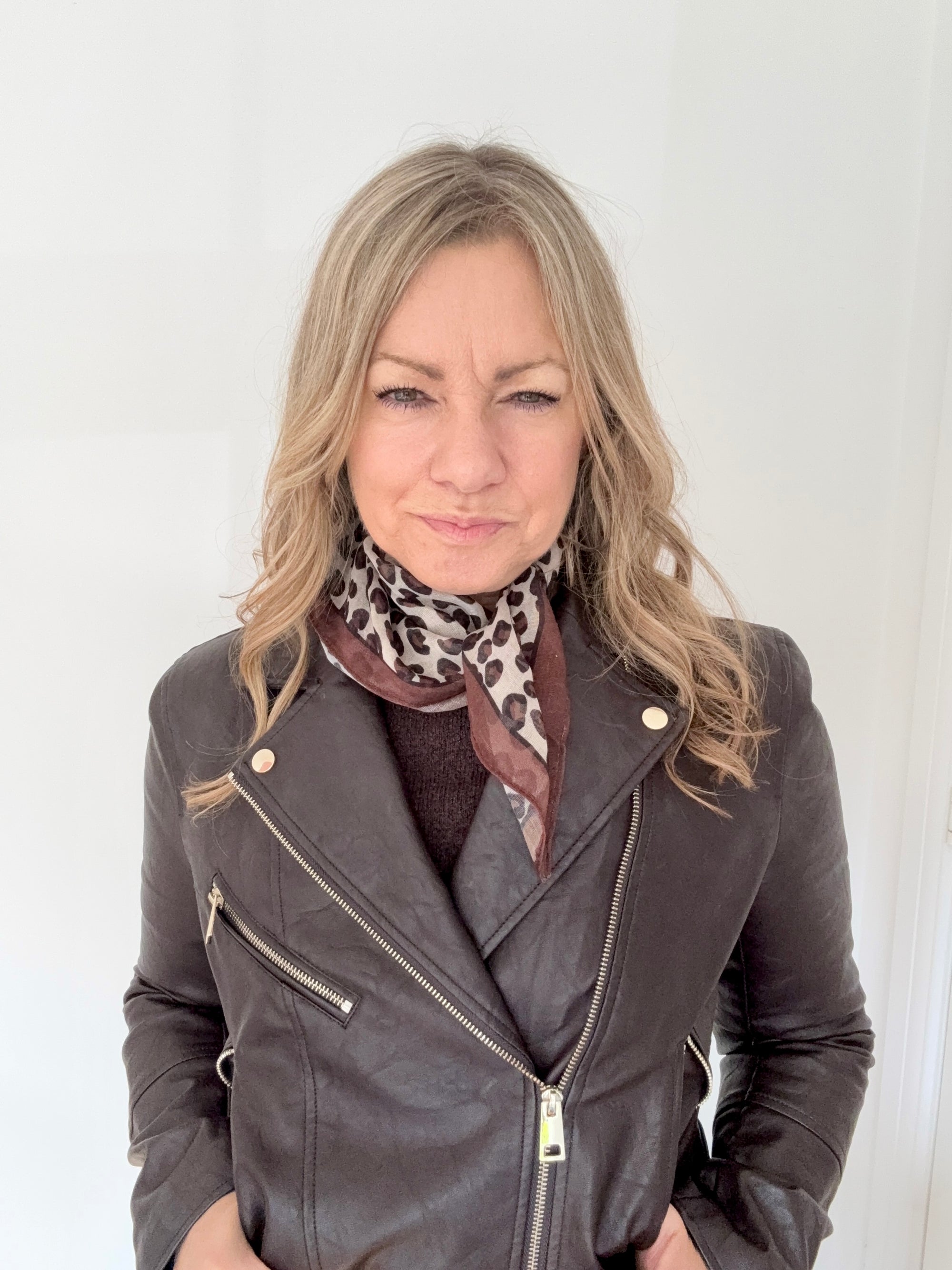 Woman wearing a grey leather jacket with a taupe animal print square scarf. 