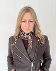 Woman wearing a grey leather jacket with a taupe animal print square scarf. 