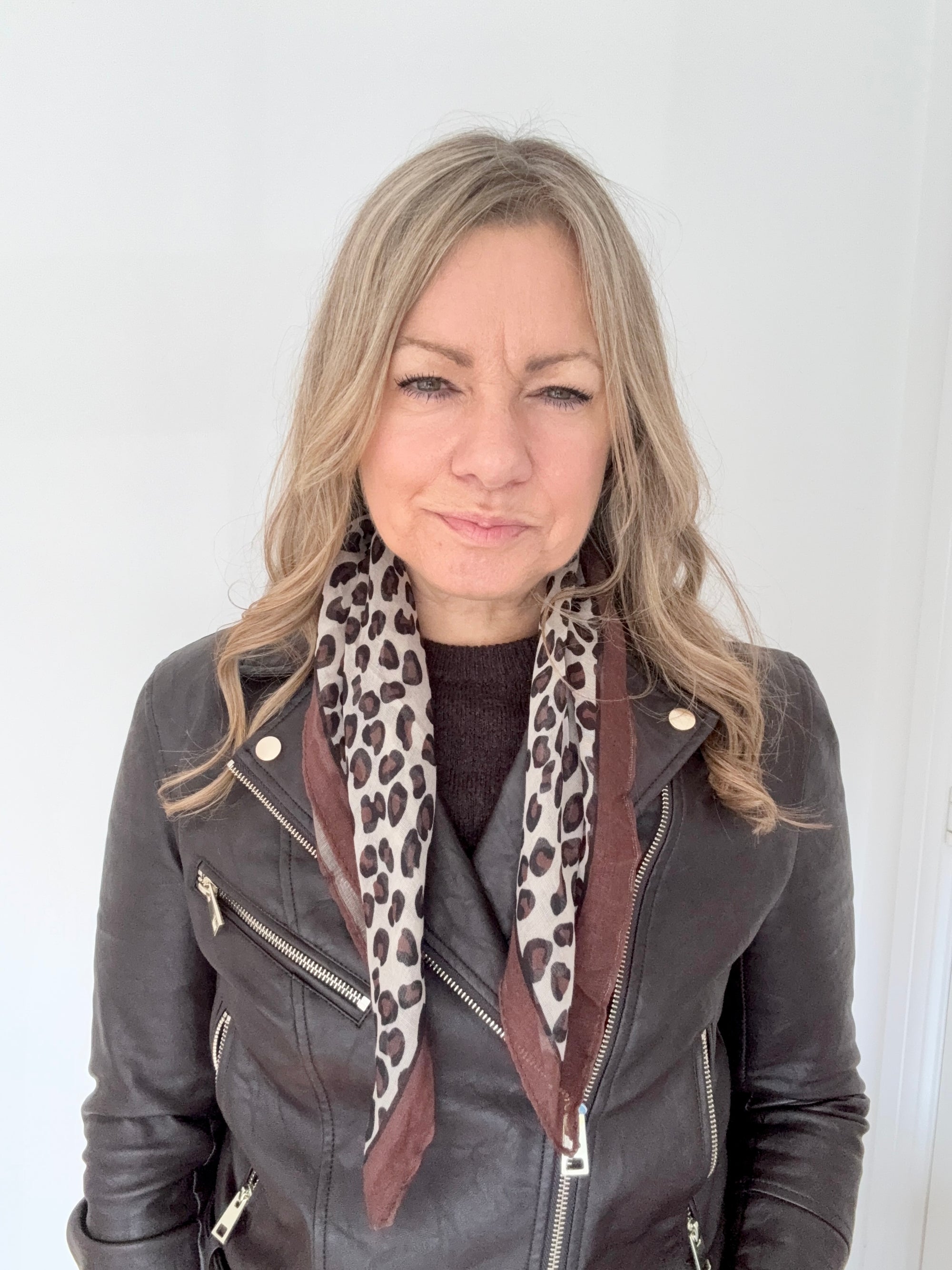 Woman wearing a grey leather jacket with a taupe animal print square scarf. 