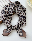 Animal print square scarf on a white surface with a book and plate in the background.