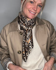 Woman wearing a beige trench coat, white sweater, and  a taupe leopard print scarf 