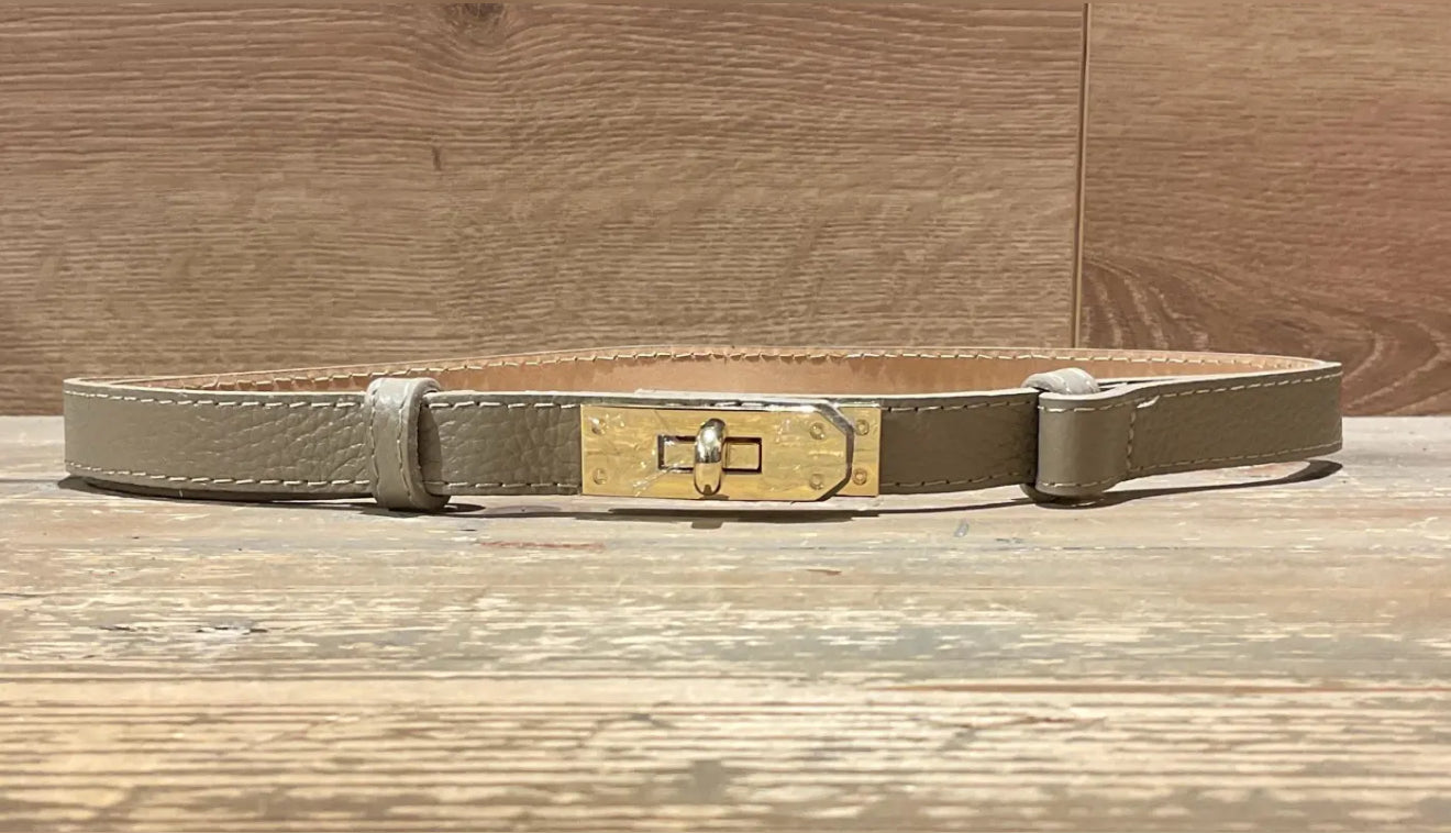 taupe narrow leather belt with a gold buckle on a wooden surface