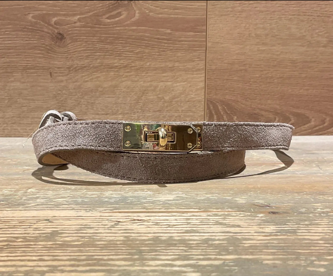 taupe suede narrow  belt with gold buckle on a wooden surface