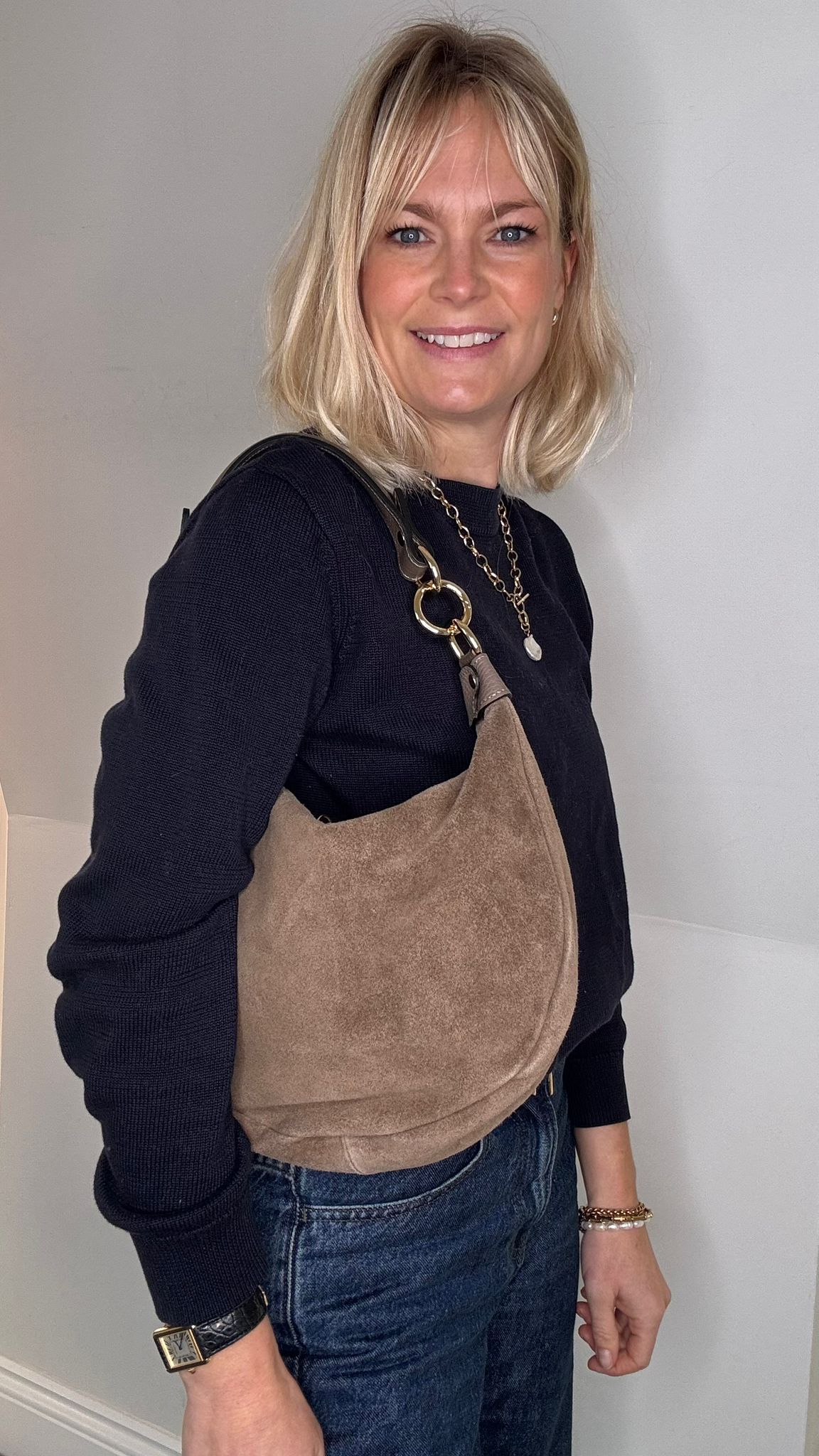 Woman wearing a black top and blue jeans with a taupe suede crossbody/ shoulder bag 