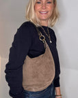 Woman wearing a black top and blue jeans with a taupe suede crossbody/ shoulder bag 