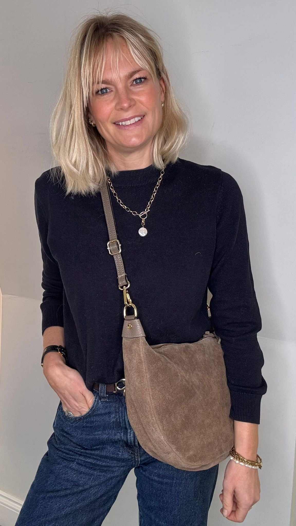 Woman wearing a black top and blue jeans with a taupe suede crossbody/ shoulder bag 