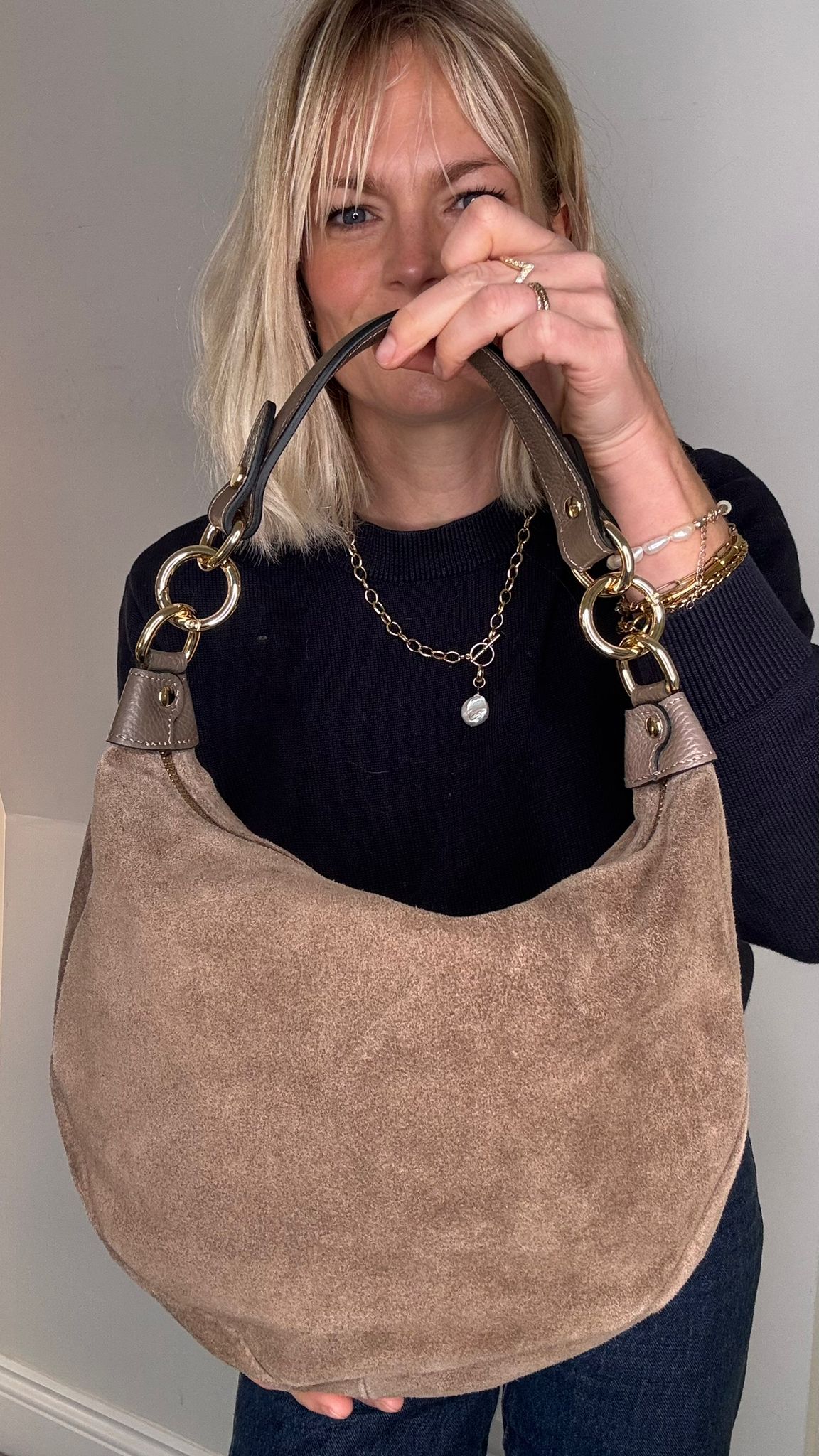 Woman holding a taupe suede crossbody/ shoulder handbag with gold hardware 