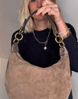 Woman holding a taupe suede crossbody/ shoulder handbag with gold hardware 