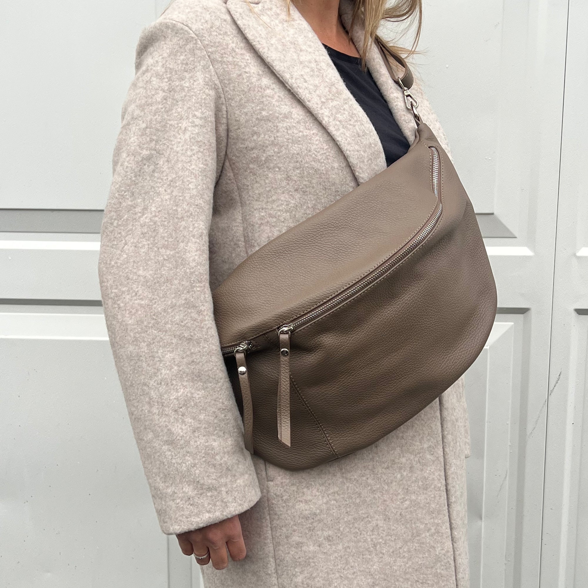 A woman wearing an XL taupe crossbody bag with silver hardware and an adjustable strap.