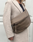 A woman wearing an XL taupe crossbody bag with silver hardware and an adjustable strap.