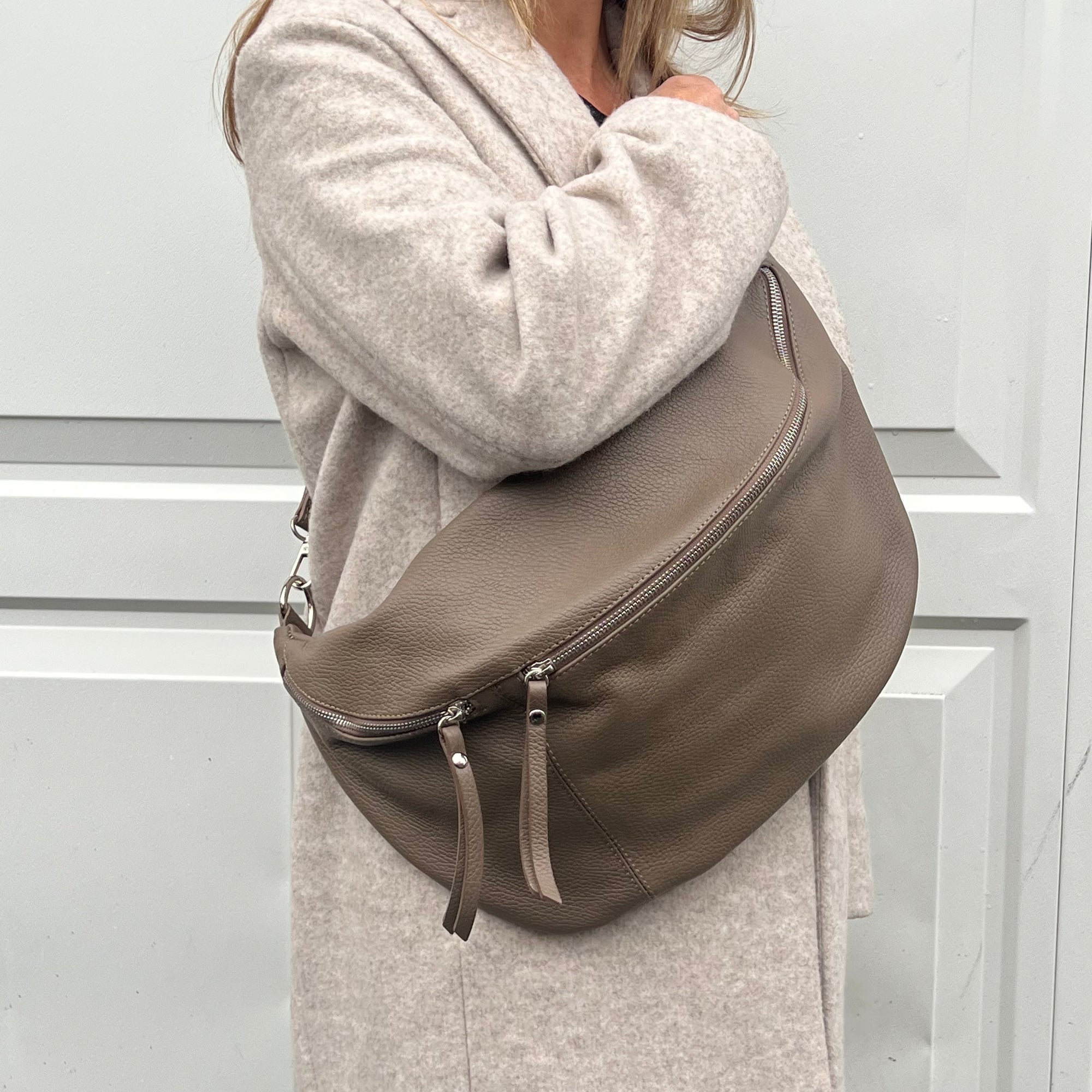 
A woman wearing an XL taupe crossbody bag with silver hardware and an adjustable strap.
