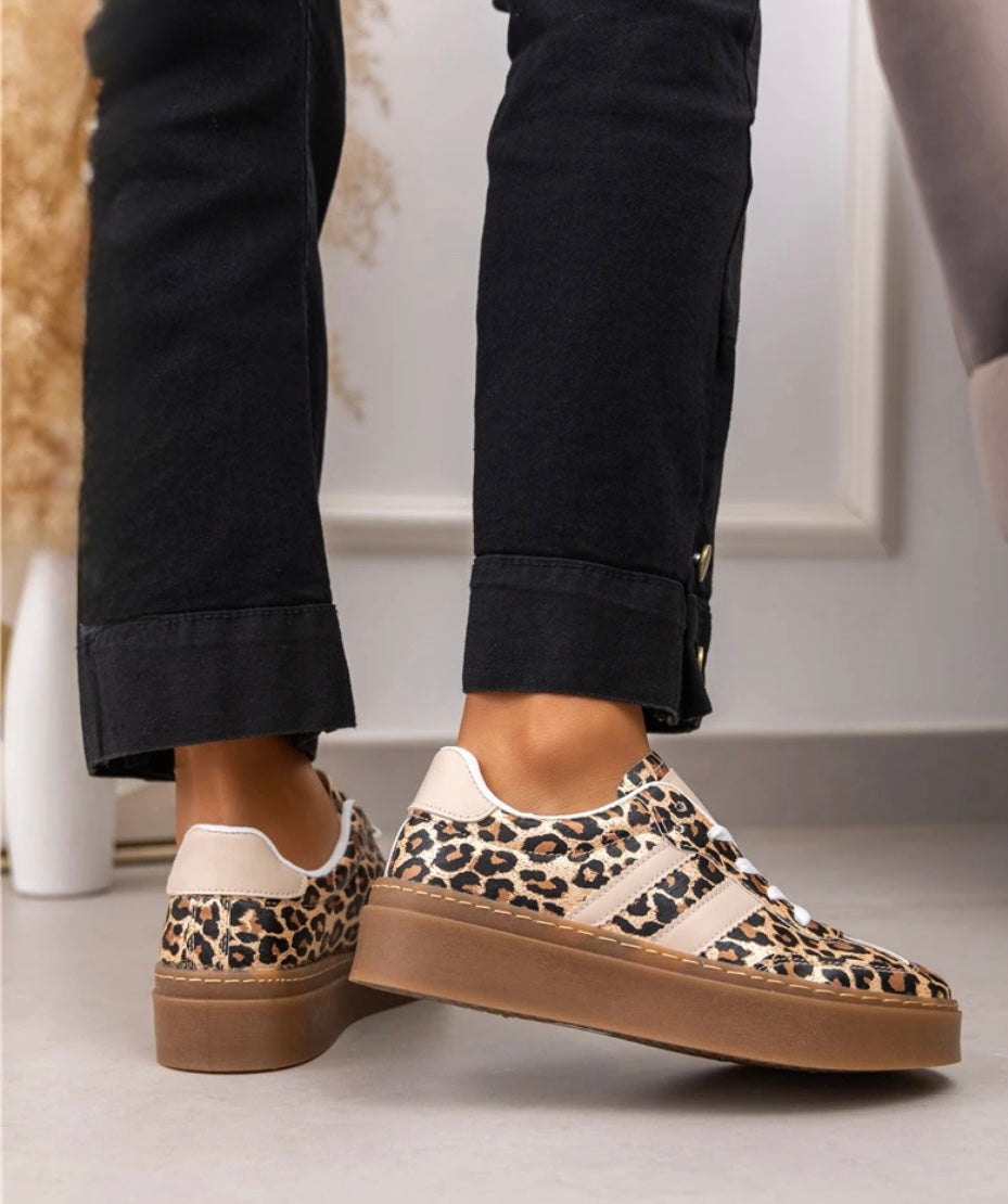 A pair of leopard print wedge lace-up trainers with two side stripes, worn by a person with black pants.