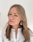 Woman wearing a white shirt and white, pink and gold beaded disc earrings. 