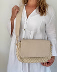 Woman holding a beige zig-zag crossbody bag 