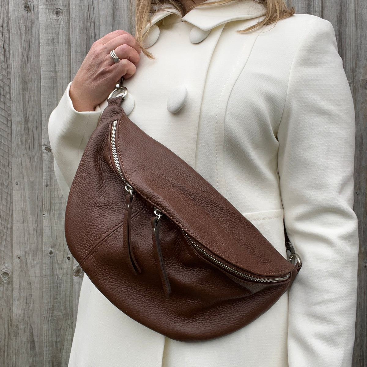 A woman wearing a brown large crossbody bum bag with an adjustable, detachable leather strap and multiple zip pockets.