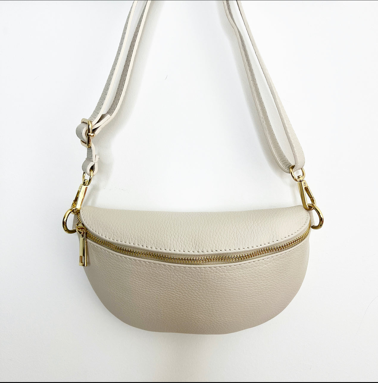 a cream crossbody / waist bag with an adjustable strap and gold hardware. 
