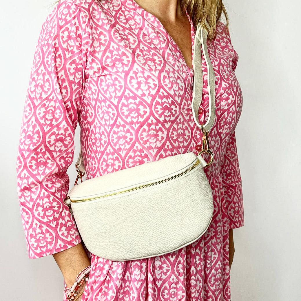 A person wearing a pink dress with a geometric pattern carrying a large cream leather crossbody bag with a detachable strap.