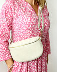 A person wearing a pink dress with a geometric pattern carrying a large cream leather crossbody bag with a detachable strap.