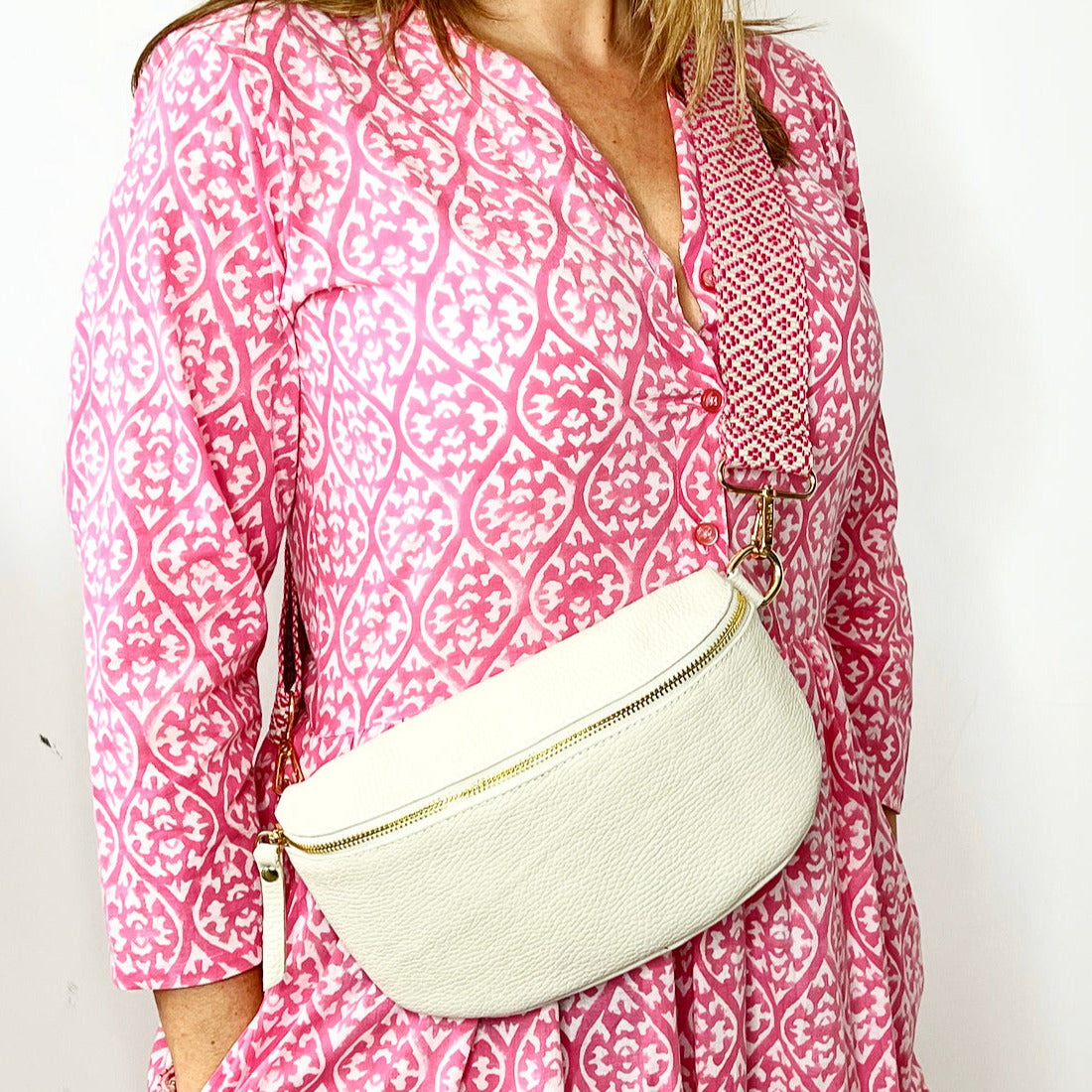 a woman wearing a large cream crossbody/ waist bag with and adjustable strap and gold hardware.
