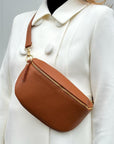 A large dark tan leather crossbody/waist bag with gold-colored hardware. 