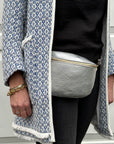 A woman  wearing a silver crossbody waist bag with an adjustable strap, standing in front of a white background.
