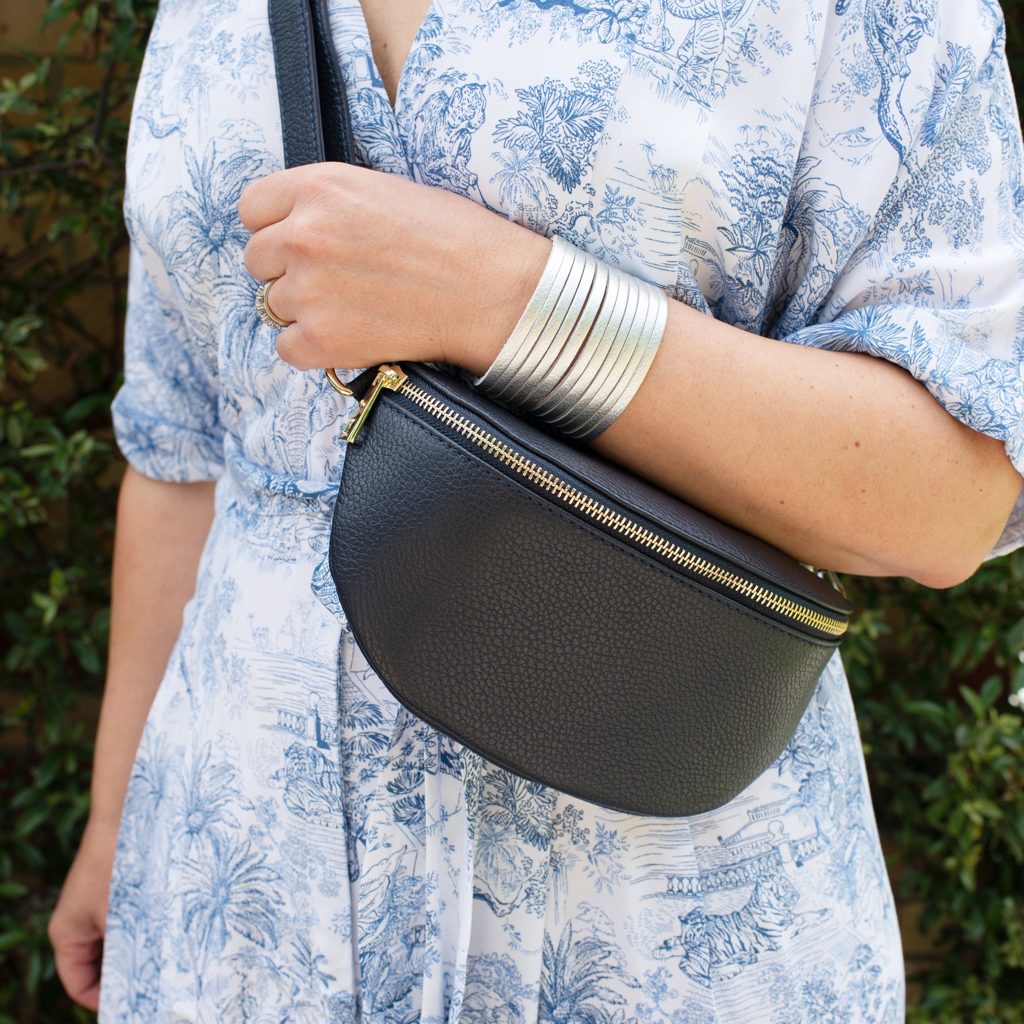 a woman wearing a navy crossbody /waistbag with gold hardware. 